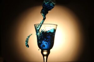Blau schimmernde Flüssigkeit wird in ein Kelchglas gegossen